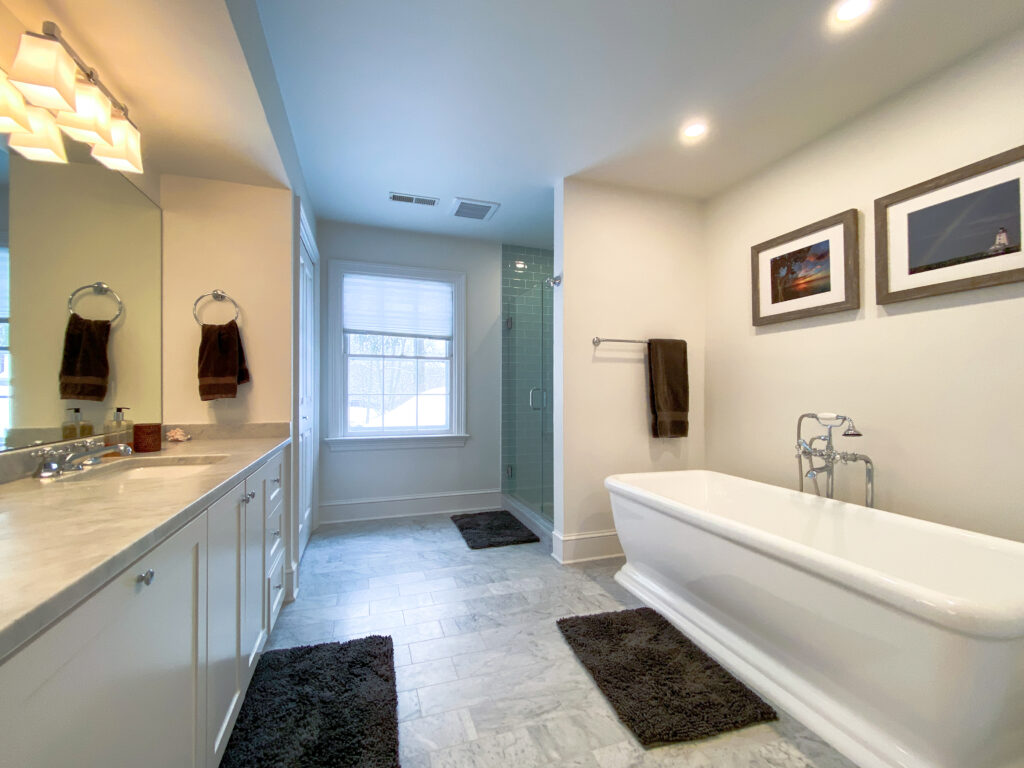 Bathroom with a white freestanding tub, a white vanity with a marble counter, a glass shower and a gray tile floor