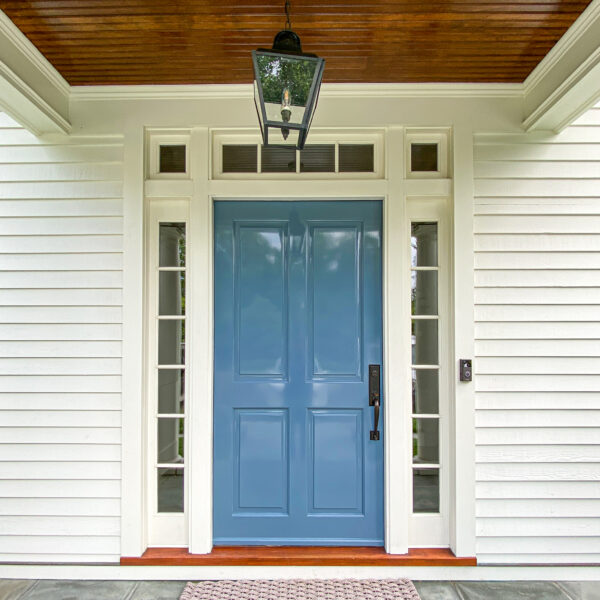 Glossy blue paneled front door with glass sidelights and a transom under a stained wood porch ceiling