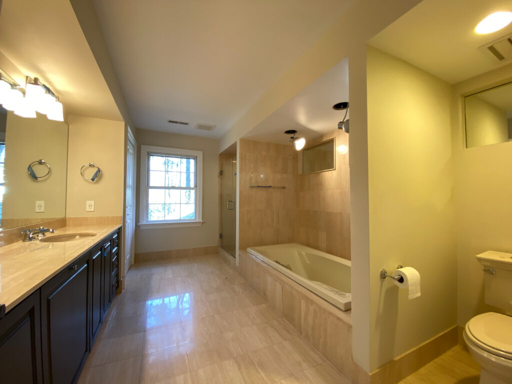 Long bathroom with a dark wood vanity, beige countertop, tiled tub surround, tile floor and a window