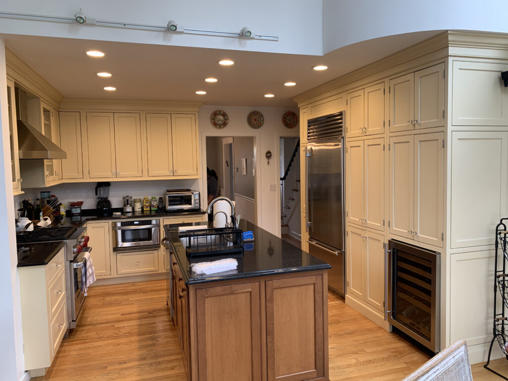 Kitchen with cream cabinets, a wood island with a dark countertop, a stainless fridge and recessed lights