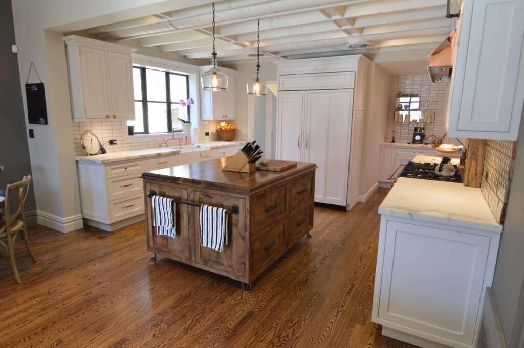 White kitchen with a reclaimed wood island, pendant lights, a beamed ceiling and dark hardwood floors