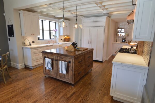 White kitchen with a reclaimed wood island, pendant lights, a beamed ceiling and dark hardwood floors