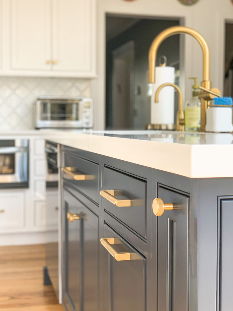 Dark navy kitchen island with brass pulls and a white countertop, with a brass faucet and white cabinets behind