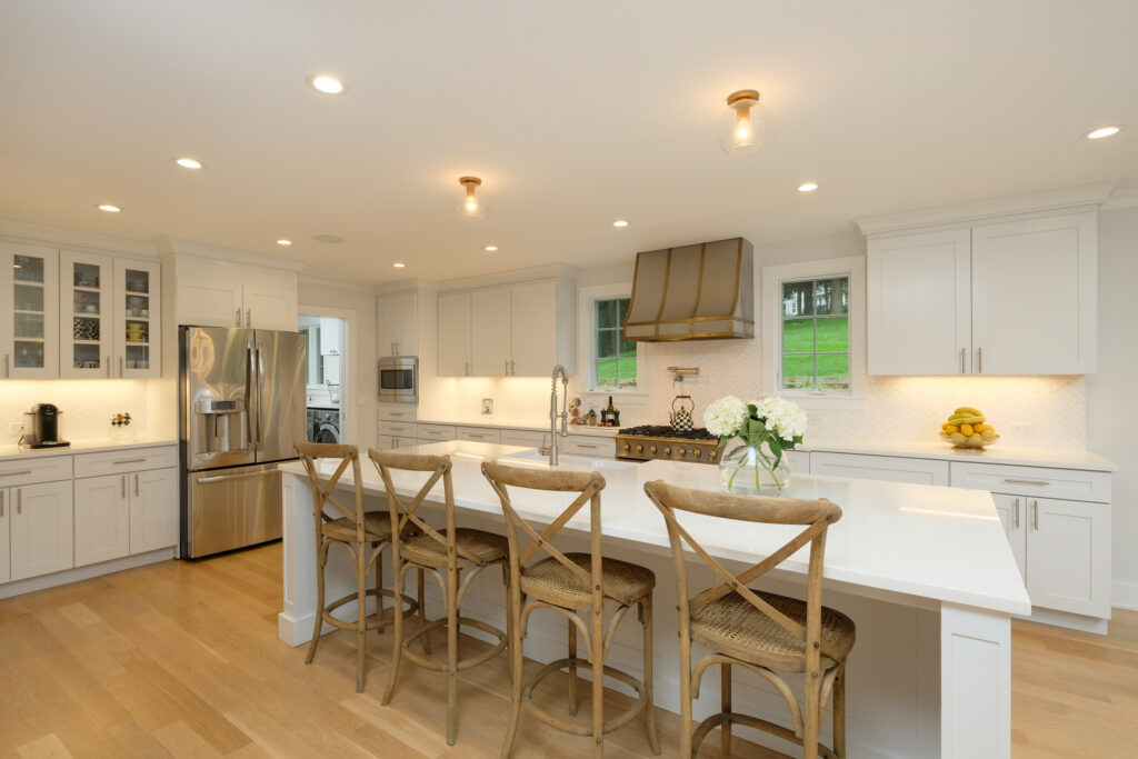 White kitchen with a long island, cross-back wood stools, glass-front cabinets and a metal range hood