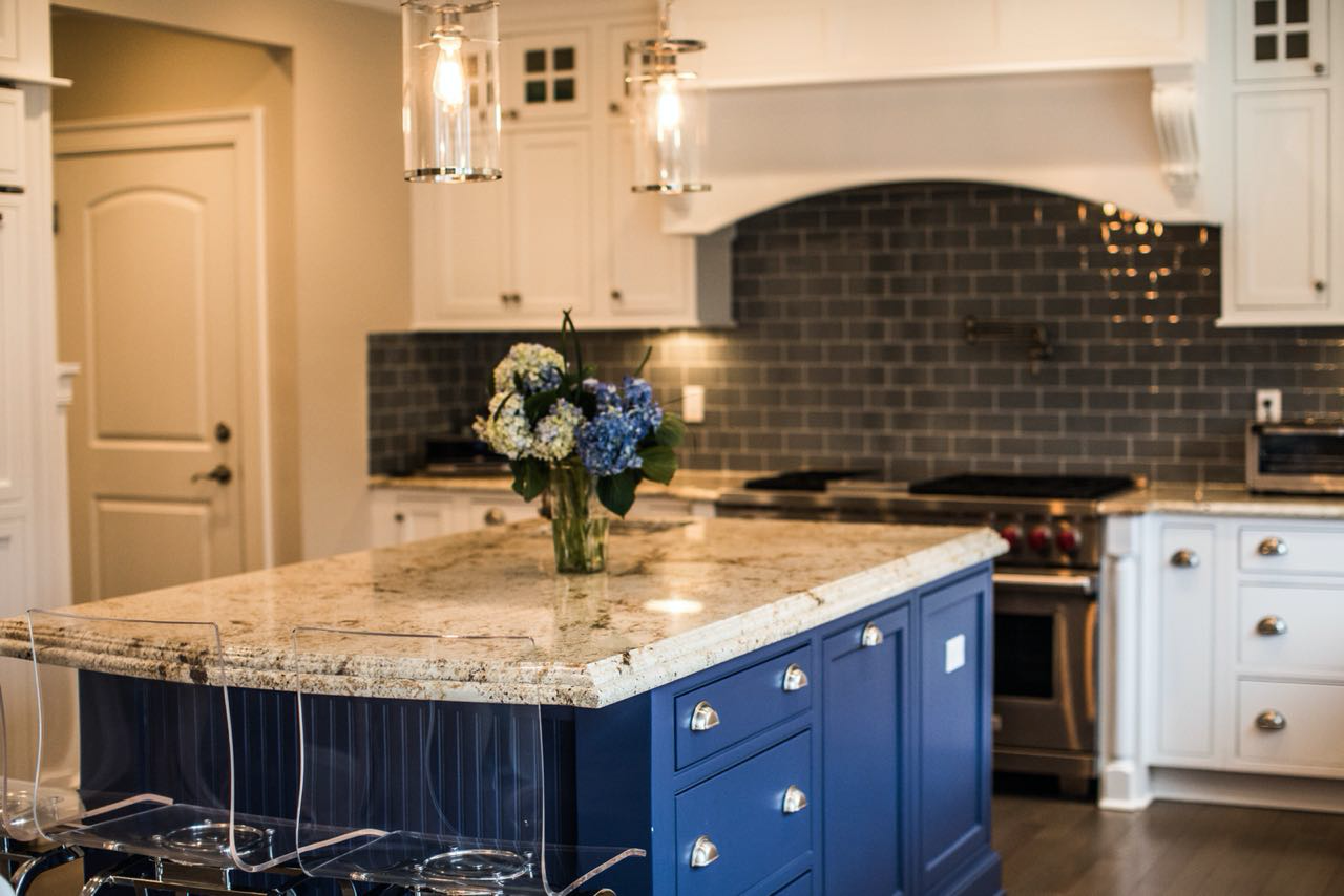 Kitchen with a navy blue island, a granite countertop, white cabinets and a dark gray subway tile backsplash