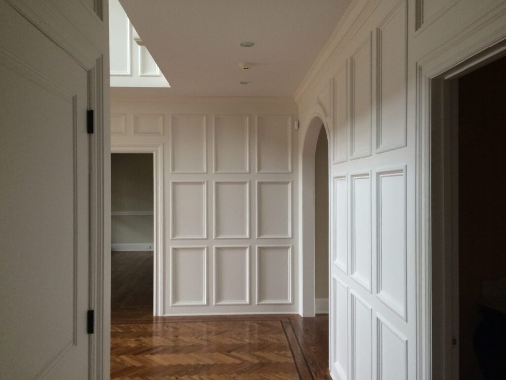 Hallway with floor-to-ceiling white raised panel walls, an arched doorway and a polished parquet wood floor