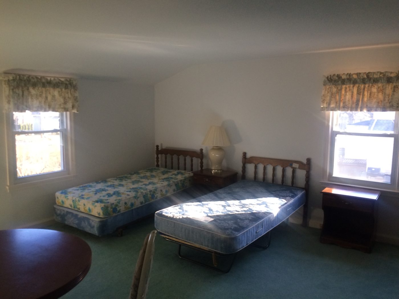 Bedroom with teal carpet, two twin beds with bare floral mattresses and floral window valances
