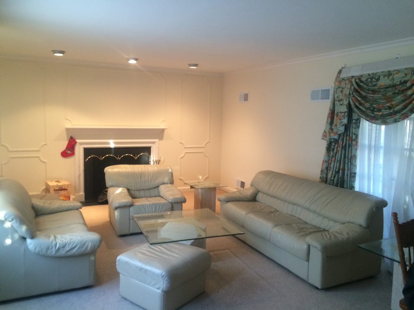 Living room with cream walls, pale leather sofas, a glass coffee table, light carpet and floral valance curtains