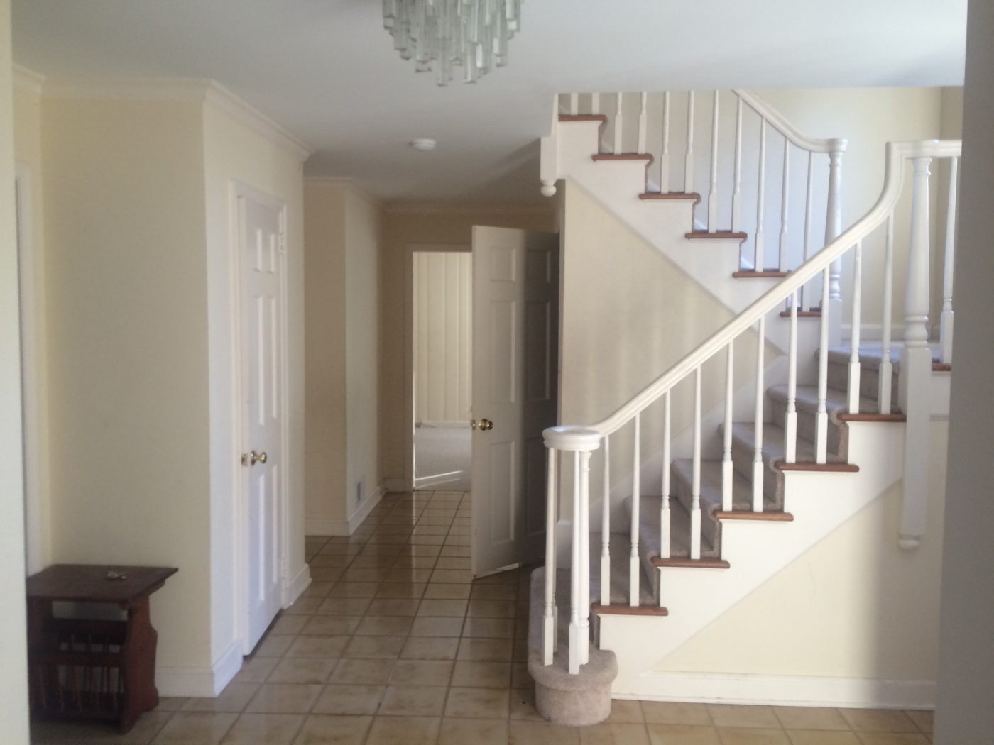 Entry hall with beige square floor tiles, a white staircase with carpeted treads and cream walls