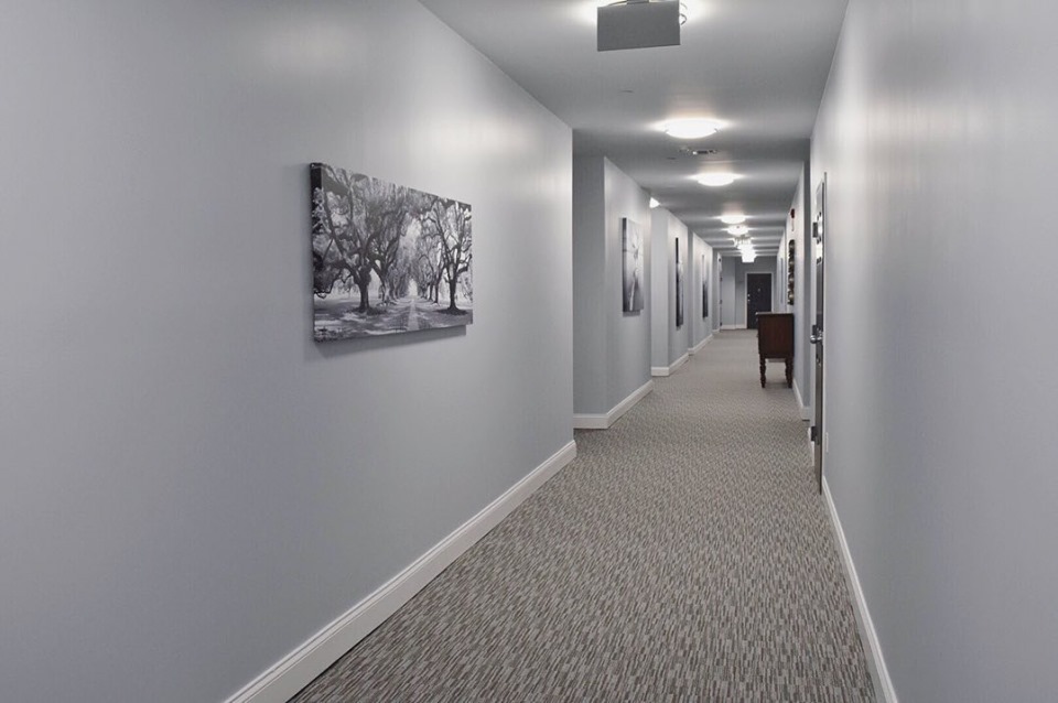 Apartment building hallway with light gray walls, white baseboards, patterned carpet and black and white canvas art