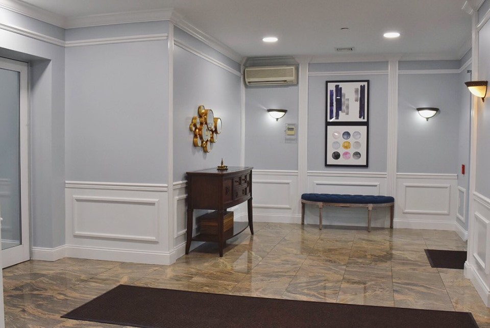 Building lobby with pale blue gray walls, white wainscoting panels, a navy tufted bench and polished stone floors