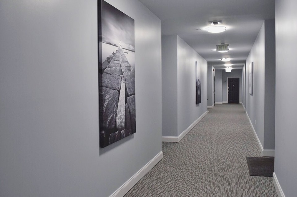Apartment hallway with light gray walls, white baseboards and a tall black and white print of a stone jetty