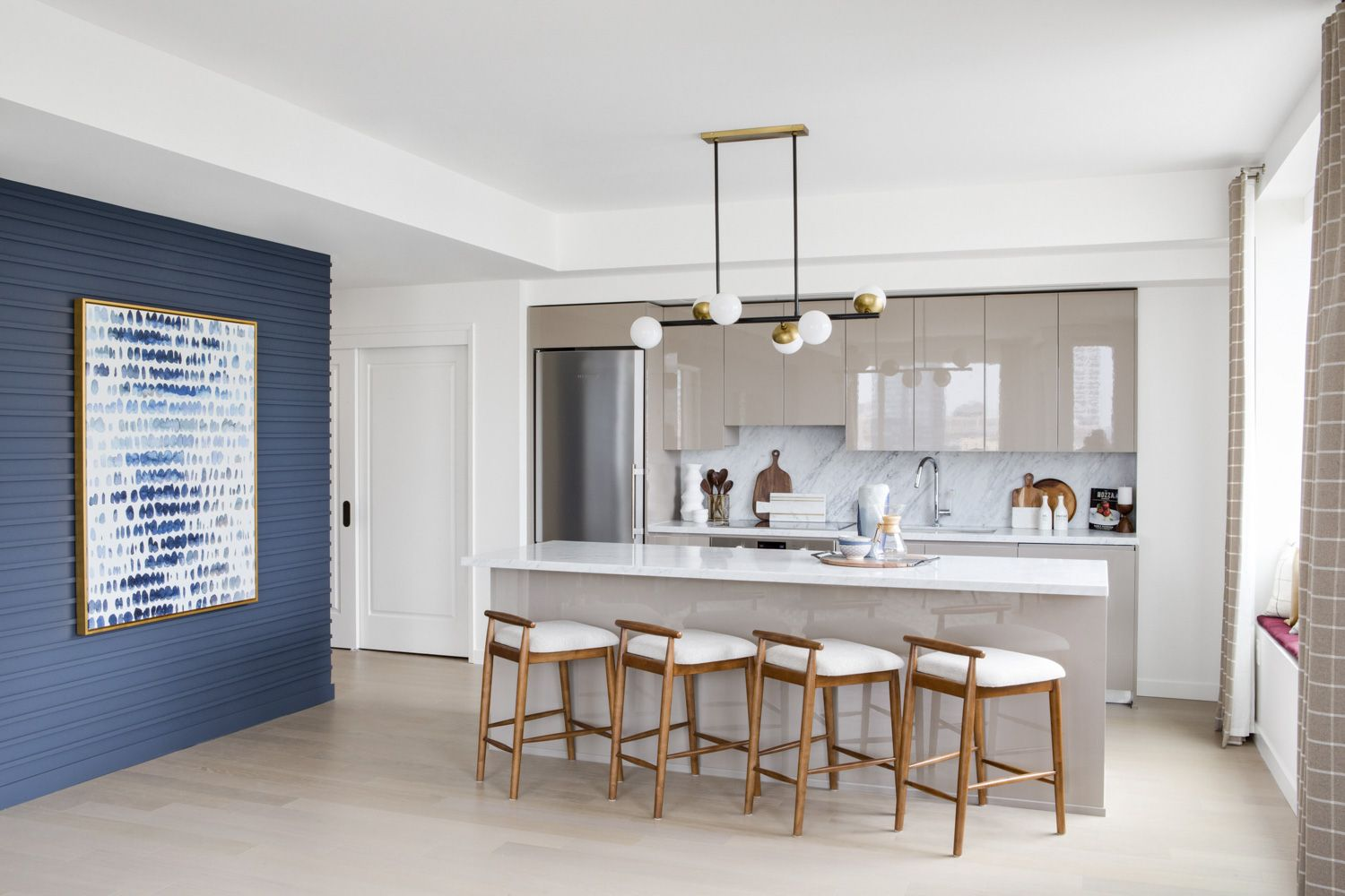 Open kitchen with glossy gray cabinets, a marble island with four wood stools and a navy shiplap accent wall