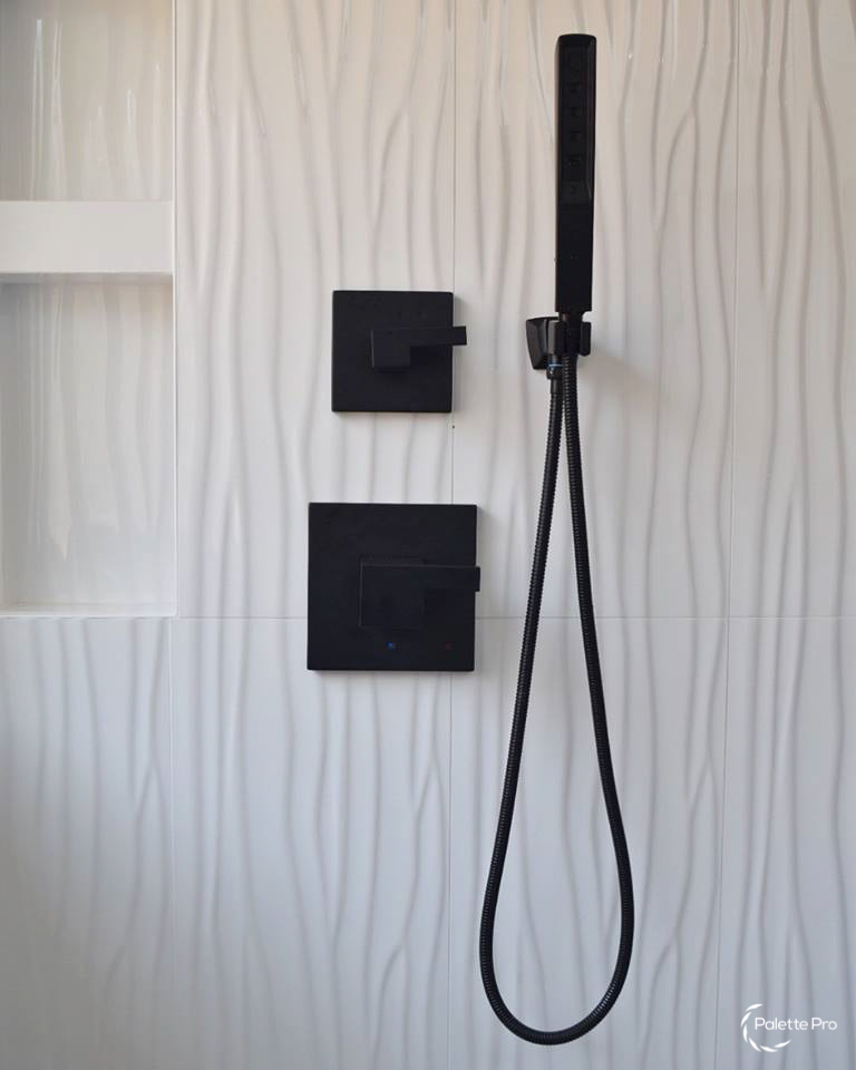 Matte black shower controls and a handheld shower head on white wavy textured wall tile