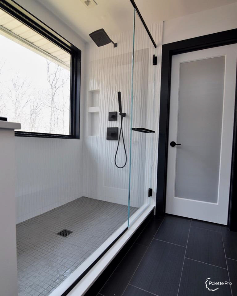 Walk-in shower with white wave pattern tile, a glass panel, matte black fixtures and a large black framed window