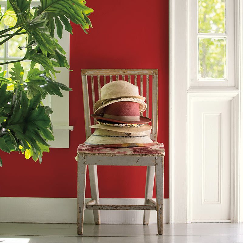 Wall in Benjamin Moore's 2018 color of the year, a deep red, behind a weathered chair stacked with straw hats