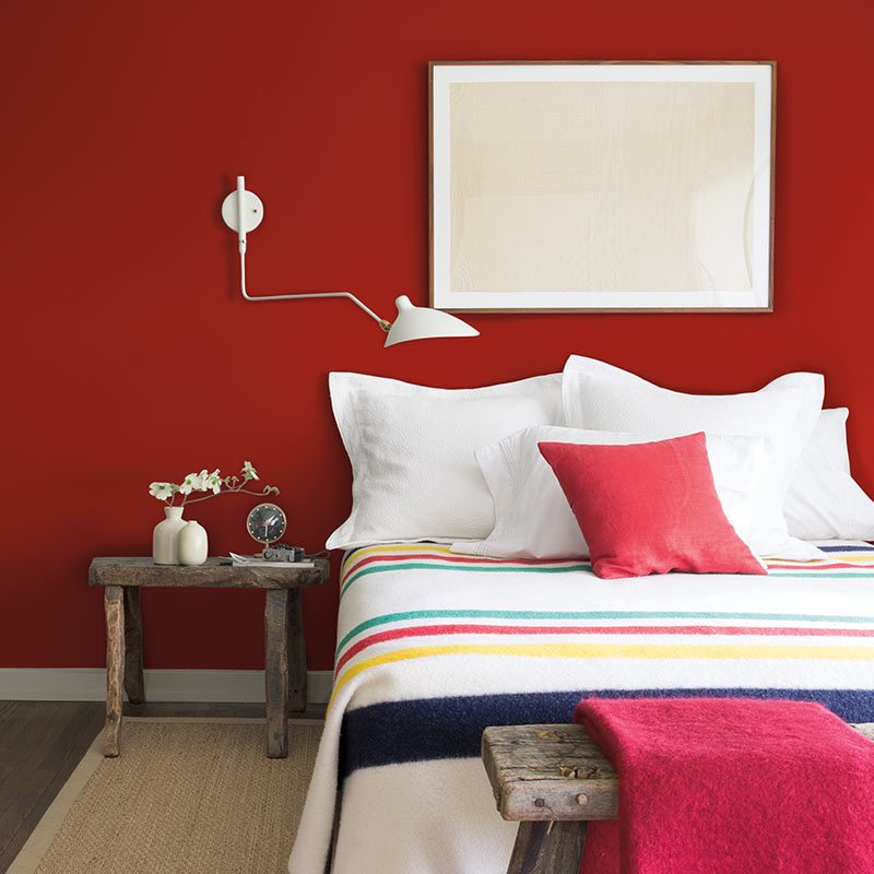 Bedroom wall in Benjamin Moore's 2018 color of the year, a deep red, above a bed with a striped wool blanket