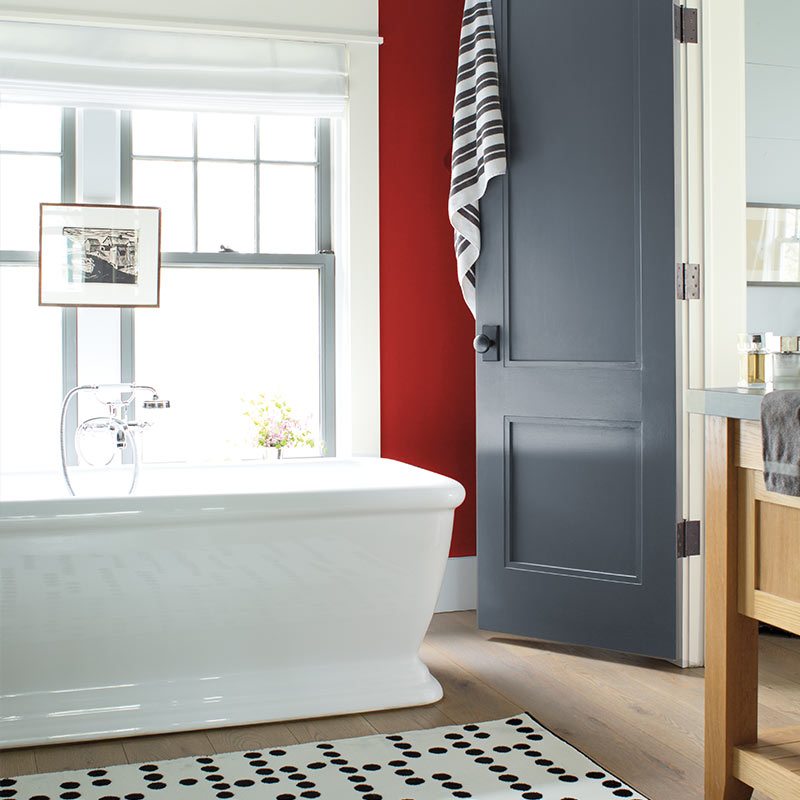 Bathroom with a freestanding tub, a wall in Benjamin Moore's 2018 color of the year, a deep red, and a gray door