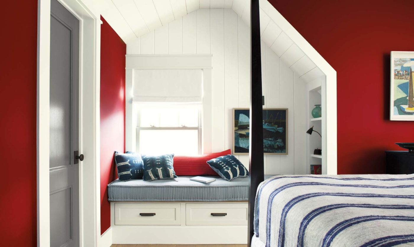 Bedroom walls in Benjamin Moore's 2018 color of the year, a deep red, around a white paneled window seat nook