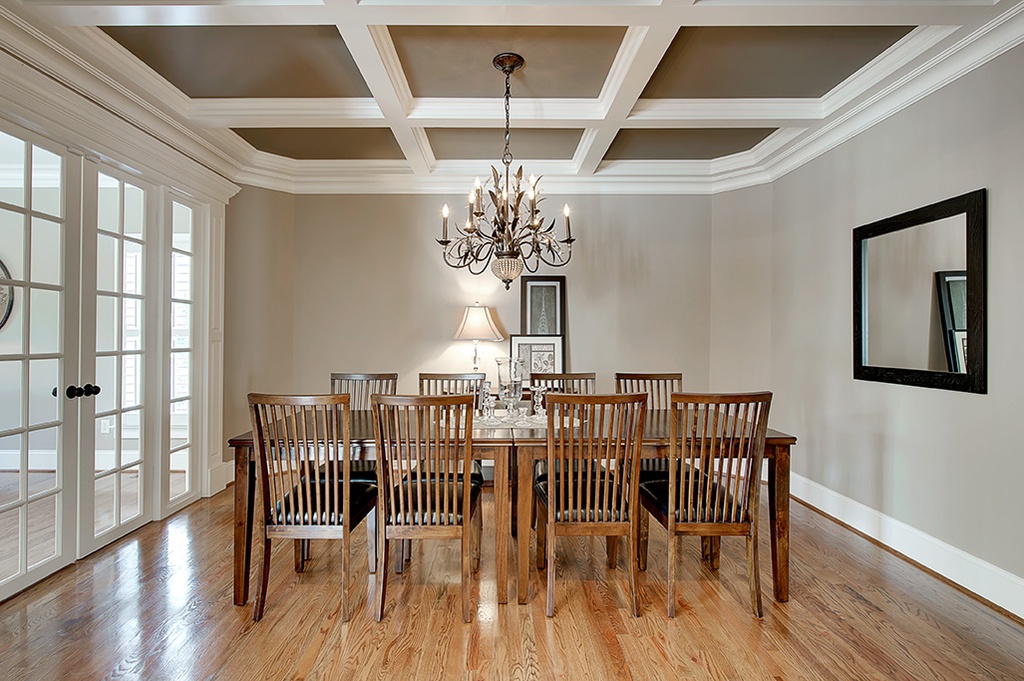 Dining room with a white coffered ceiling, greige walls, a chandelier, a wood table and chairs, and French doors