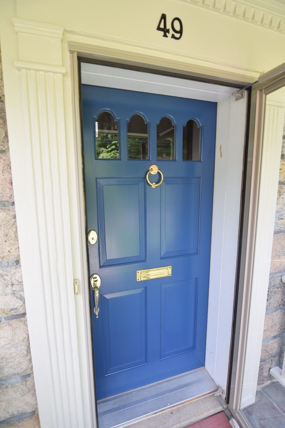 Blue paneled front door with four arched glass panes, a brass ring knocker and a brass mail slot in white trim