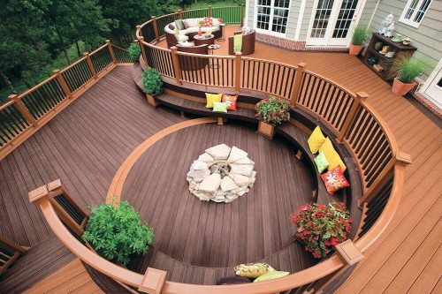 Curved multi-level deck with built-in bench seating, colorful pillows, planters and a round stone fire pit