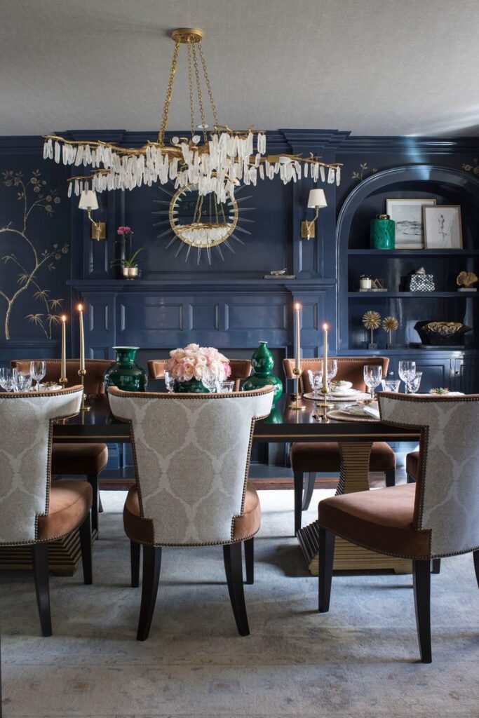Dining room with navy blue walls and built-in shelves, a crystal chandelier, upholstered chairs and a candlelit table