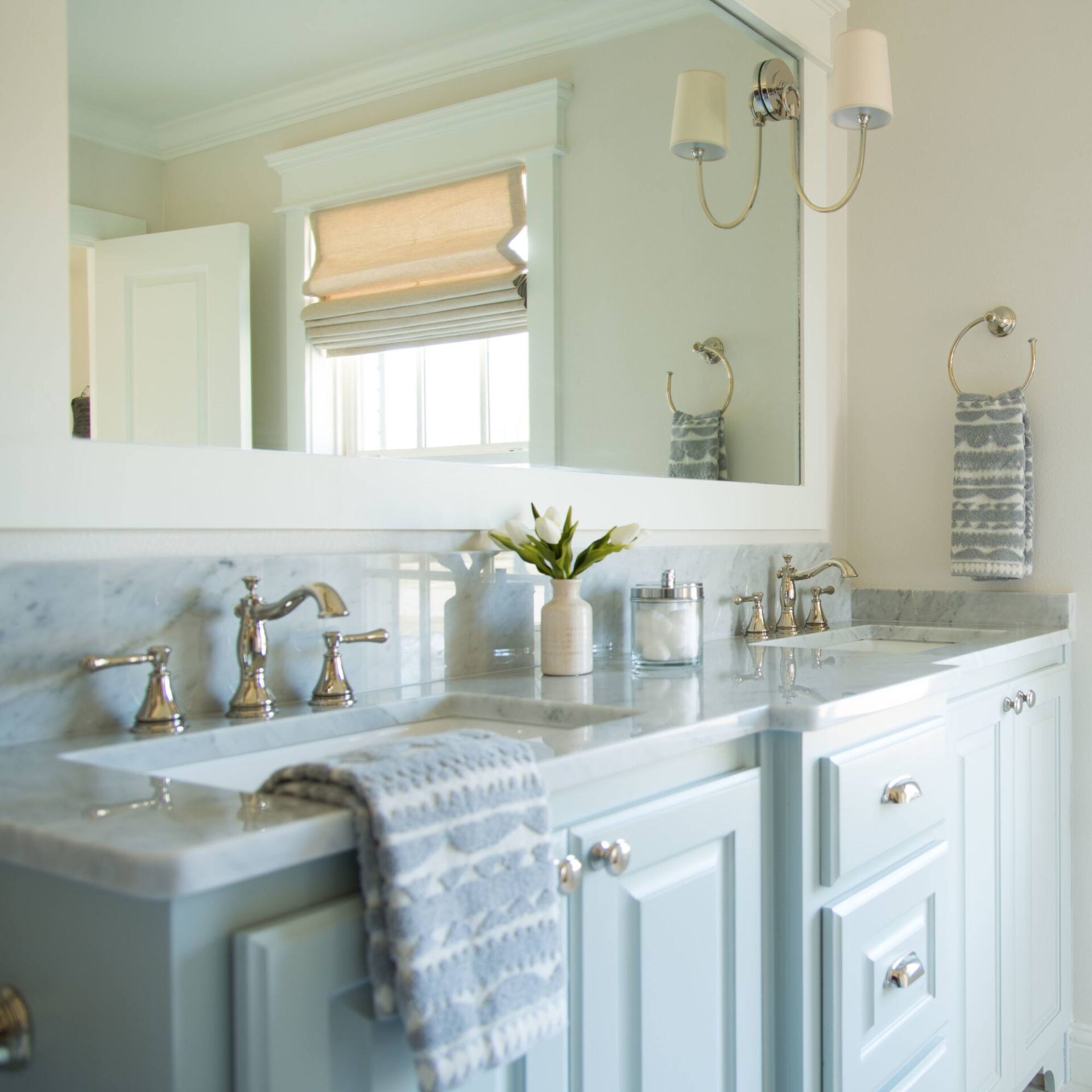 Pale blue double vanity with a marble top, polished nickel faucets, a large white-framed mirror and a two-arm sconce