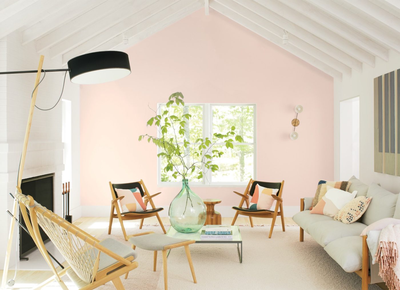Living room with a soft pink wall, a white beamed vaulted ceiling, wood lounge chairs and a light gray sofa