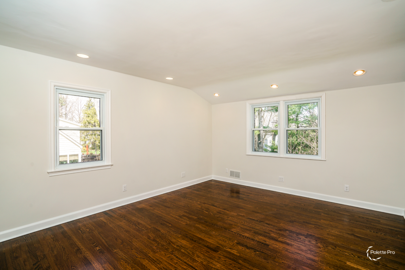 Empty bedroom with refinished dark hardwood floors, off-white walls, white trim and a sloped ceiling