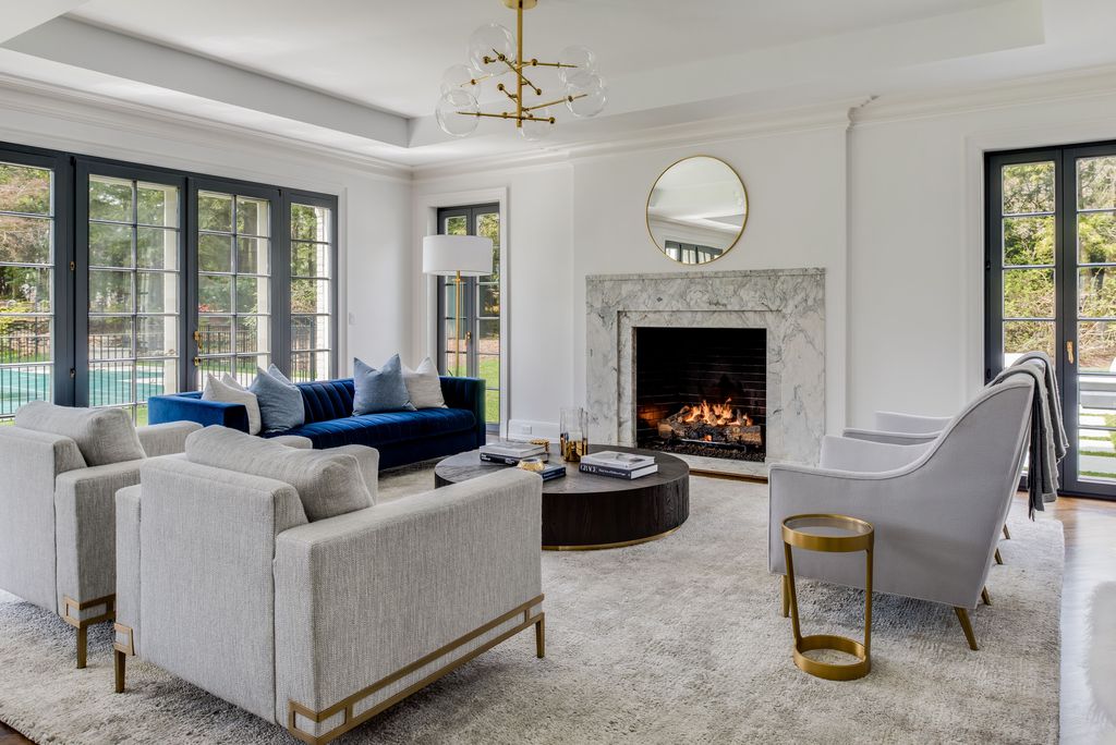 Living room with white walls, a marble fireplace, a navy velvet sofa, gray armchairs and black framed French doors