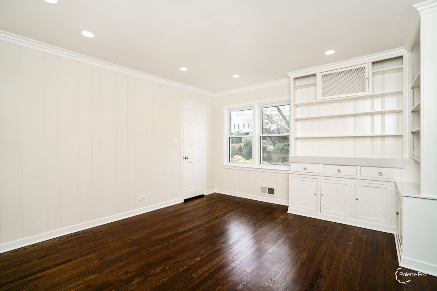 Den with white painted paneled walls, white built-in shelves and cabinets and dark hardwood floors
