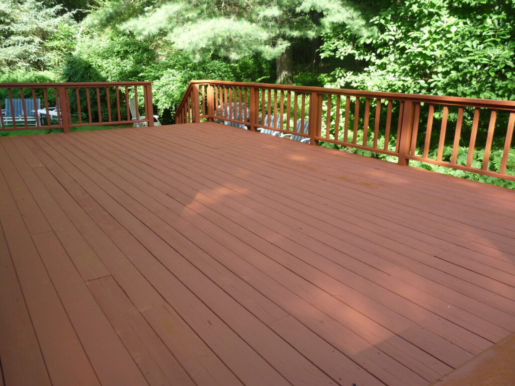 Large wood deck with a red-brown finish and matching railings, surrounded by tall trees