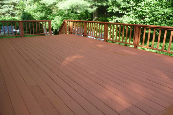 Large wood deck with a red-brown finish and matching railings, surrounded by tall trees