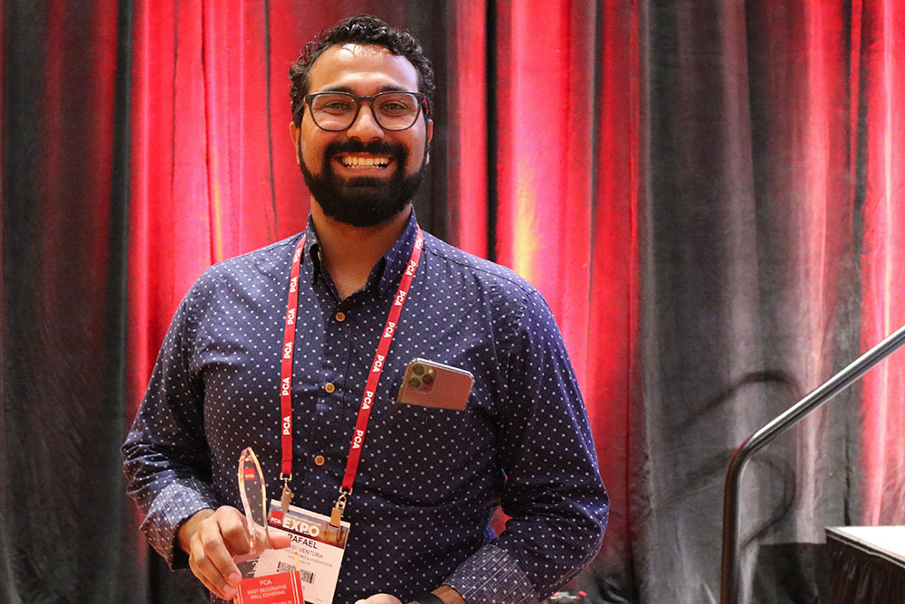 Team member with a PCA Expo badge holding a Best Decorative Wall Covering award in front of a red curtain