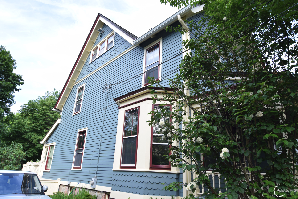 Side of a Victorian house painted blue-gray with cream trim, burgundy window sashes and a bay window