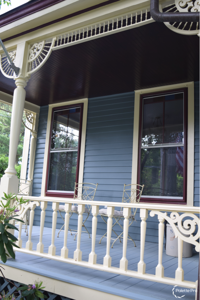 Victorian front porch with cream turned balusters and fretwork brackets, blue-gray siding and burgundy sashes