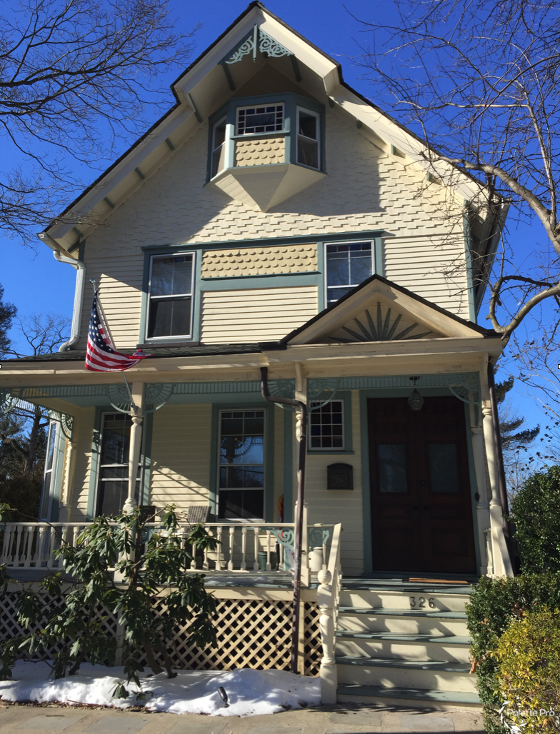 Victorian house in pale yellow with blue-green trim, scalloped shingle accents and a front porch, snow on the ground