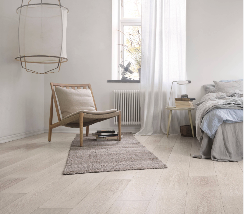 Minimal bedroom with a whitewashed wood floor, a wooden lounge chair, a woven rug and an unmade bed
