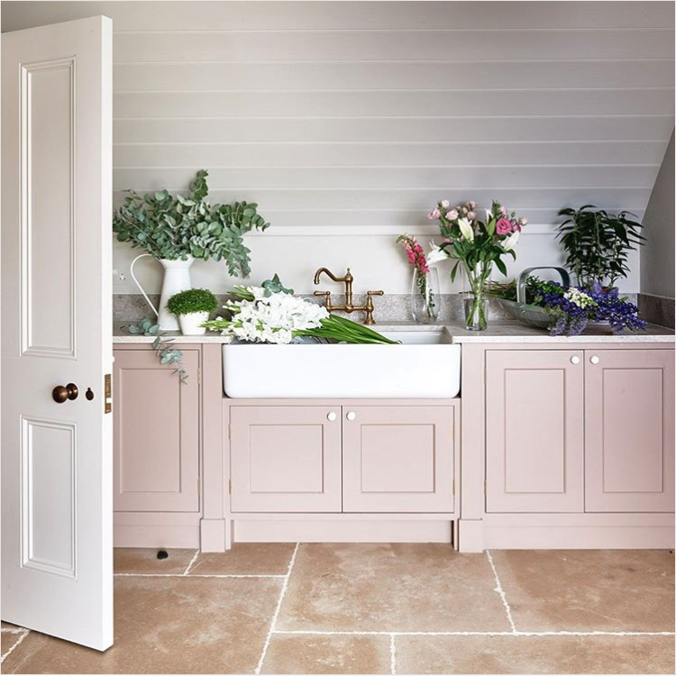Utility room with blush pink cabinets, a white farmhouse sink with a brass faucet and fresh flowers on the counter