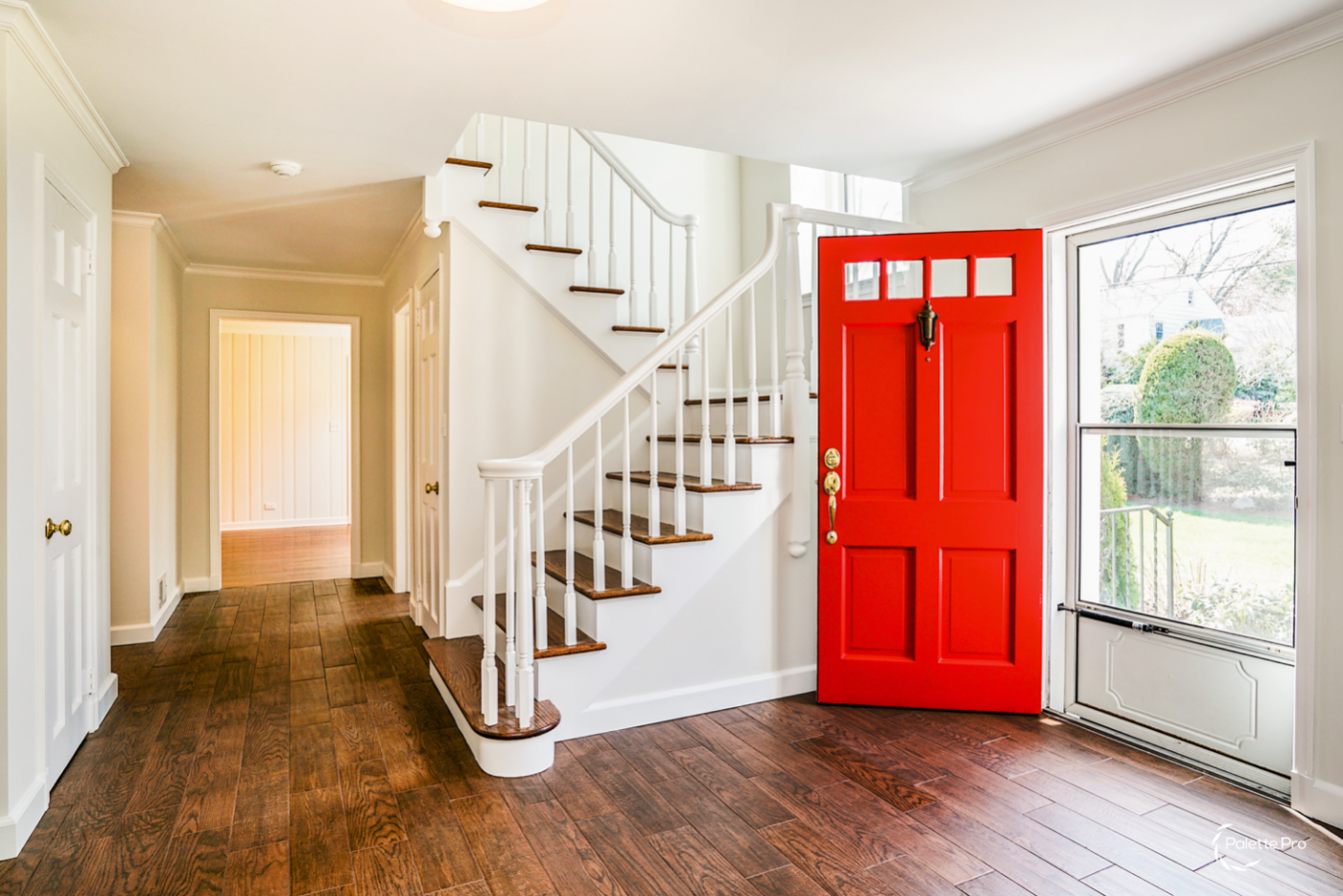 Entry hall with a bright red front door, a white staircase with wood treads and dark wood-look plank flooring