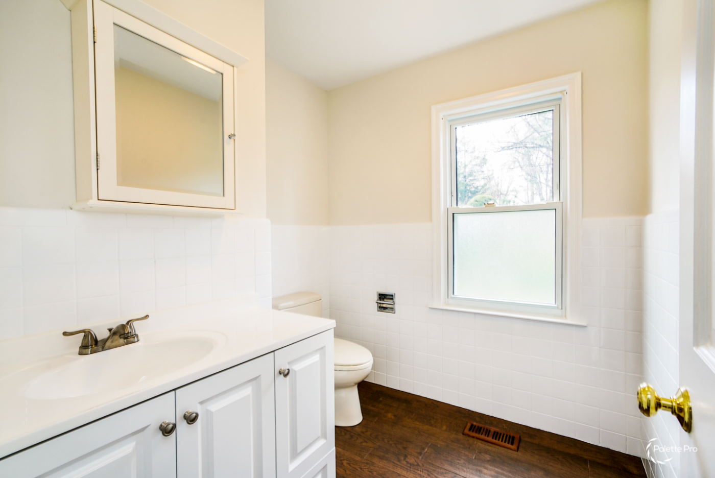 Bathroom with reglazed white wall tile, cream walls, a white vanity, medicine cabinet and dark wood-look floor