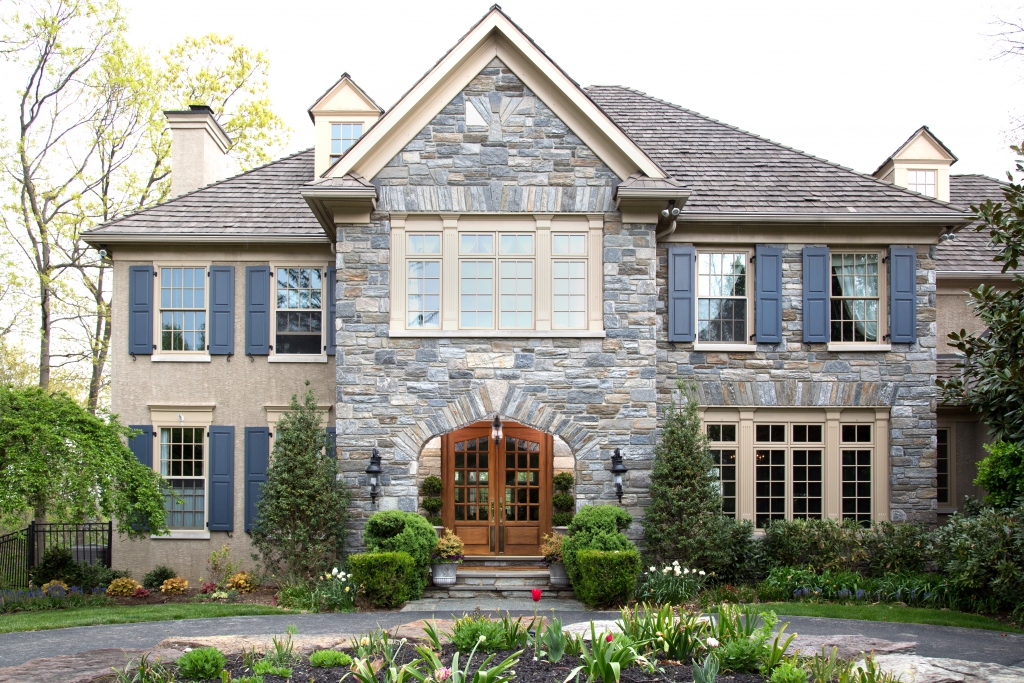 Stone and stucco house with slate blue shutters, cream trim and arched wood double front doors