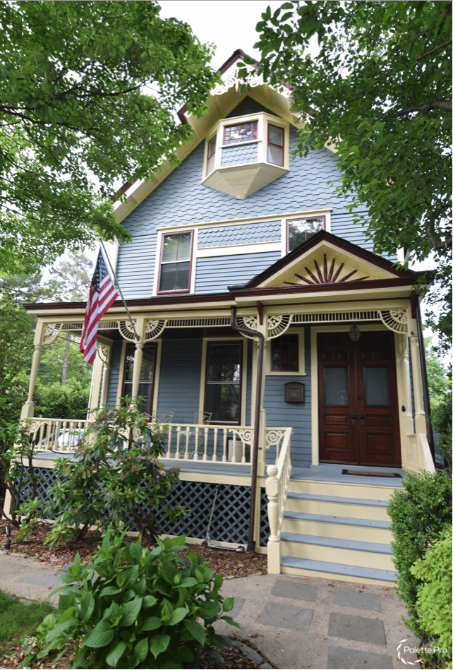 Victorian house painted blue-gray with cream trim, burgundy window sashes and a spindled front porch
