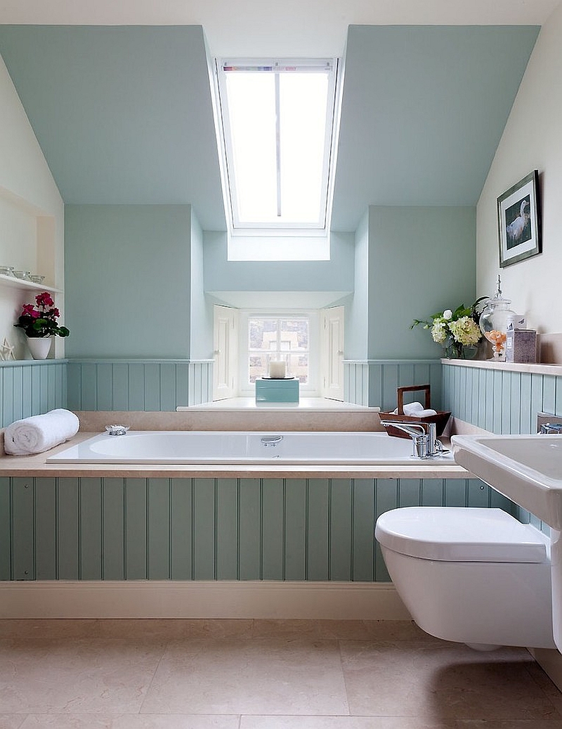Attic bathroom with pale aqua walls and beadboard, a built-in tub under a skylight and a wall-hung toilet