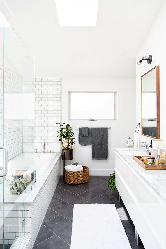 White bathroom with subway tile around the tub, dark slate floor tiles, a floating white vanity and a skylight