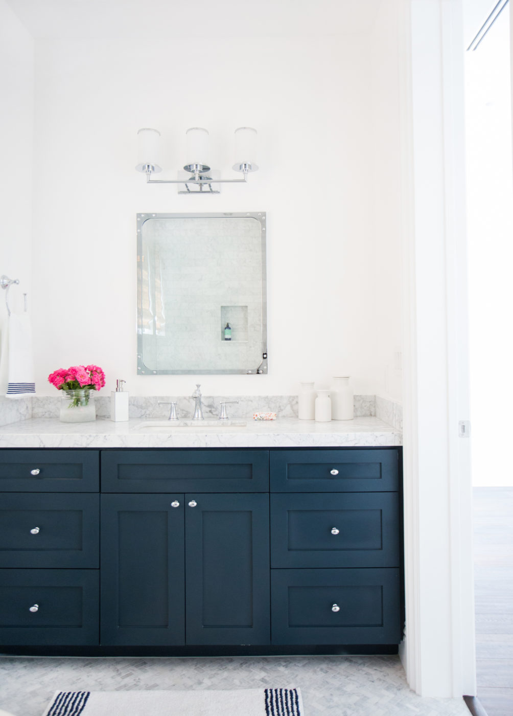Navy blue bathroom vanity with a white marble top, chrome knobs, a framed mirror and a three-light fixture