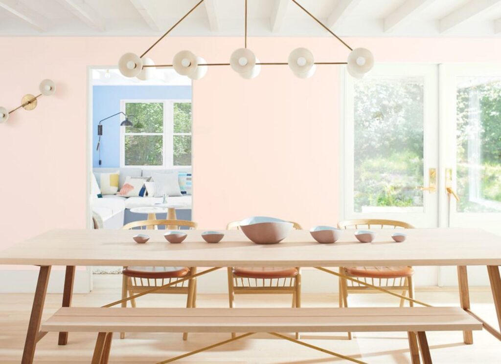 Dining room with soft pink walls, a long light wood table and bench, and a modern globe light fixture