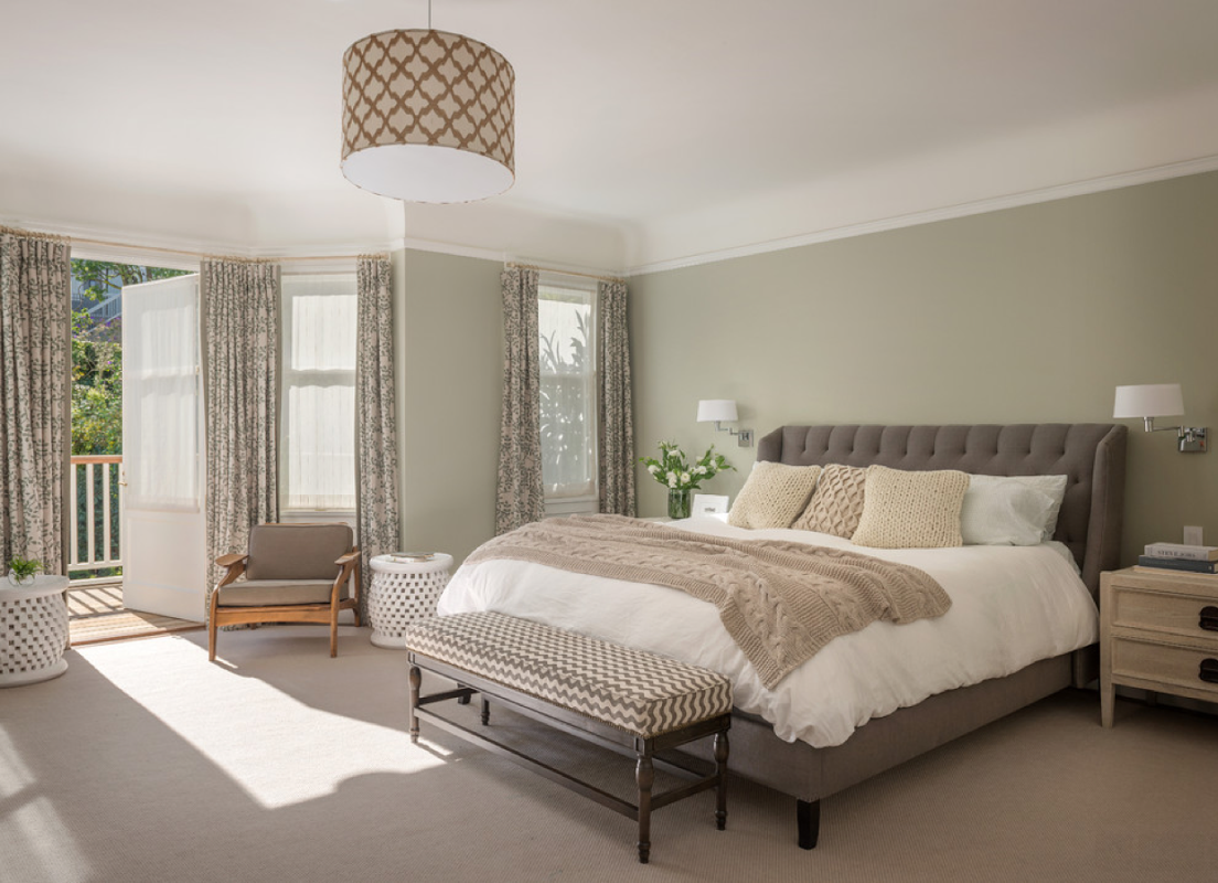 Bedroom with sage green walls, a gray tufted bed, patterned curtains, a chevron bench and a patterned drum pendant