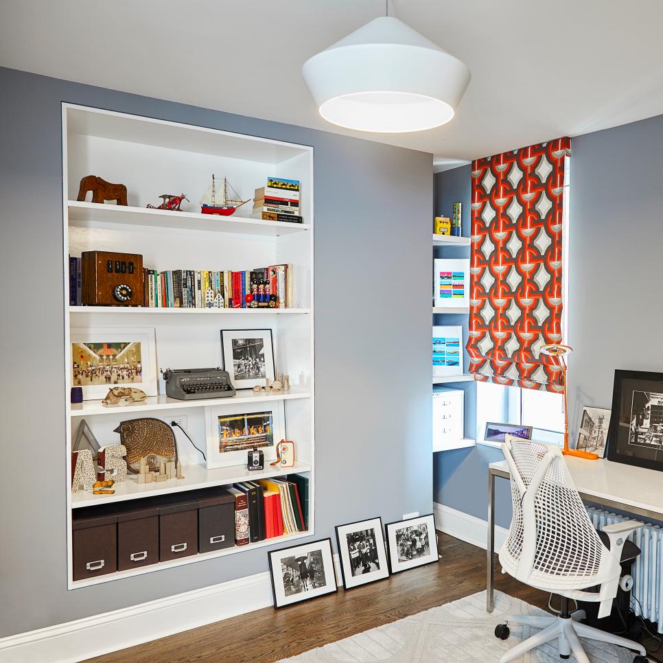 Home office with gray walls, a recessed white bookshelf, an orange patterned roman shade and a white mesh desk chair